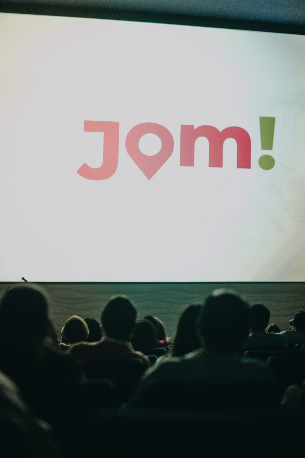 Logo de Jom! en pantalla gigante durante conferencia